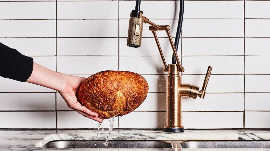 Man soaking stale loaf of bread under kitchen tap