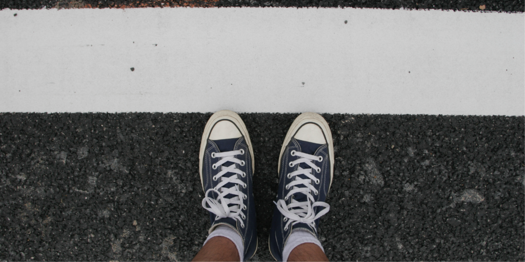 Man wearing converse with feet touching thick white line boundary on road