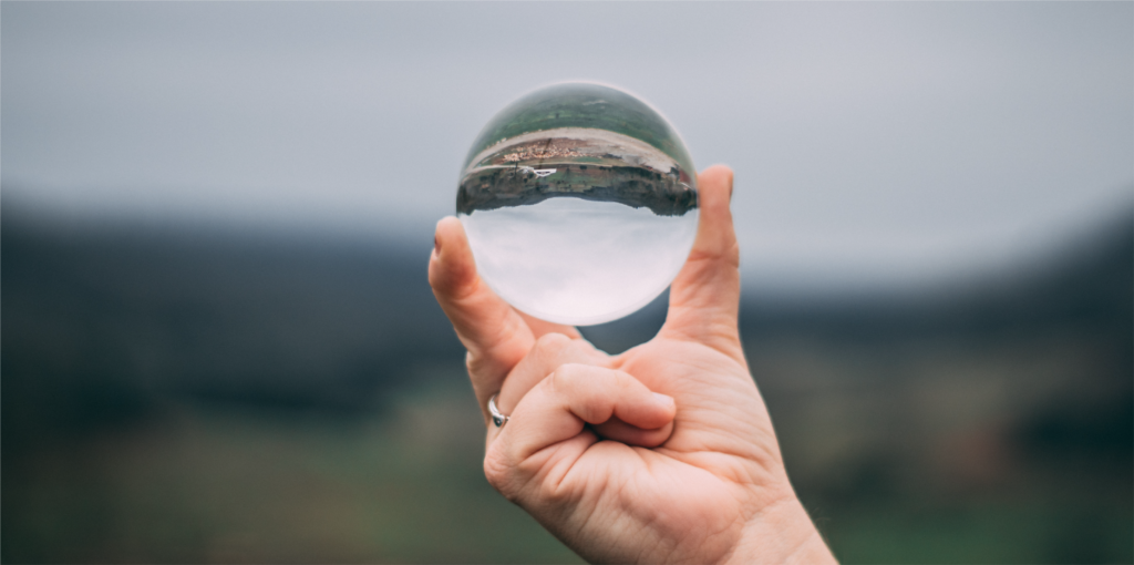 Hand holding glass ball with upside down perspective of a field captured in it